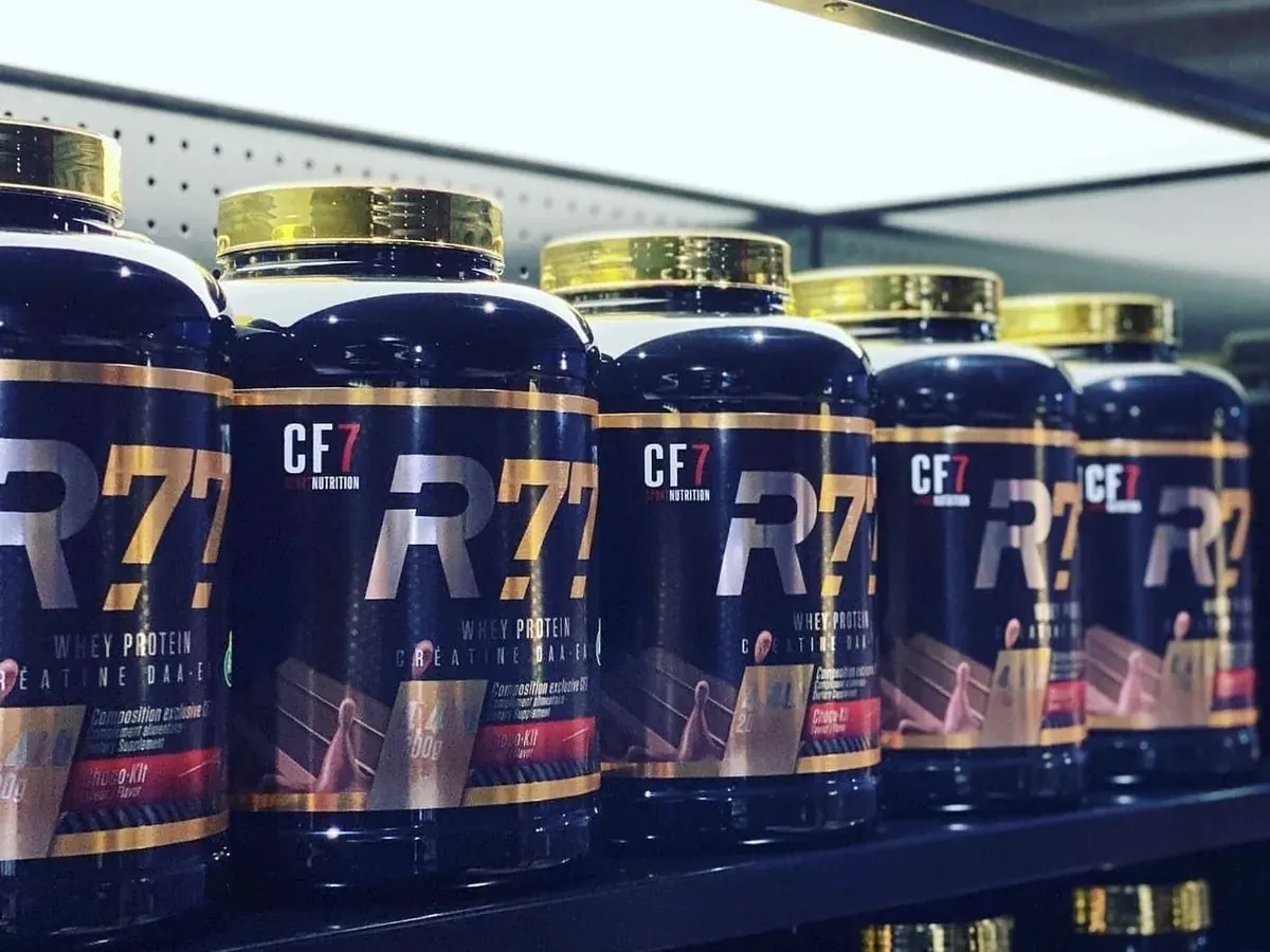 Des pots de protéine CF7 R77, couvercles dorés, alignés sur un rayon de magasin.